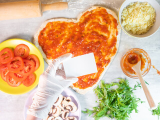 Hand holding empty business card on hear shape pizza dough background