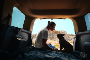 Man and french bulldog sitting in car trunk against mountain