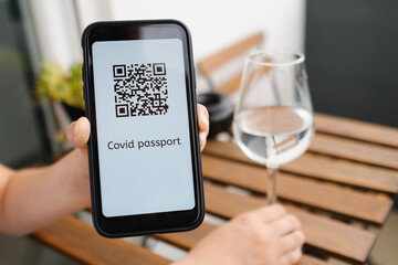 Woman demonstrates Covid pass application or digital health passport with QR code in mobile phone sitting in the cafe, 