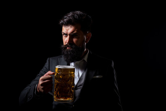Serious man in classic suit drinking beer. Bearded guy in business outfit looks happy and satisfied. Portrait of man with lifted high glass of beer on black background.