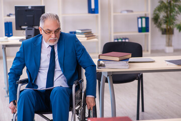 Old male employee in wheel-chair sitting in the office