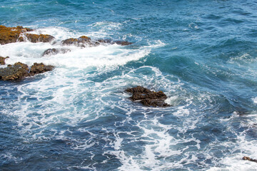 Blue sea and rocks storming. Wave spray over rocks. Rocky sea coast.
