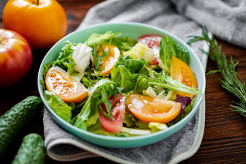 Healthy salad of fresh vegetables, herbs and tomatoes on a wooden background.