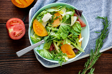 Healthy salad of fresh vegetables, herbs and tomatoes on a wooden background.