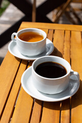 a cup of coffee and a cup of tea on a wooden table on the veranda of the house on a sunny morning