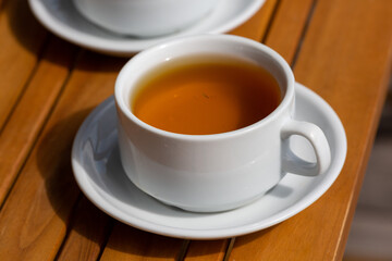 a cup of tea in a white mug and saucer on a wooden background on a sunny morning outside