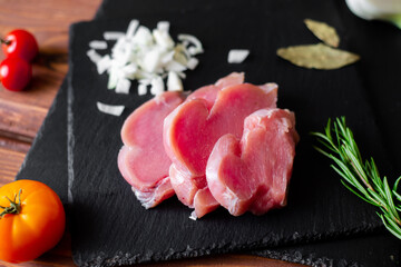 Chunks of sliced raw turkey meat, chopped onions, on a black slate background.
