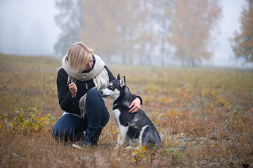 Naklejka na ściany i meble Young woman with beautiful siberian husky dog playing in city park during autumn
