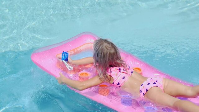 Blonde girl swims in the pool on an inflatable mattress