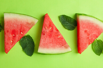 Juicy watermelon slices and leaves on green background