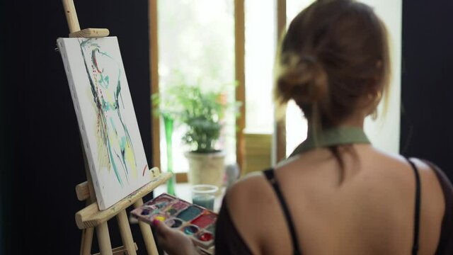 Female artist in apron painting picture on canvas in art studio