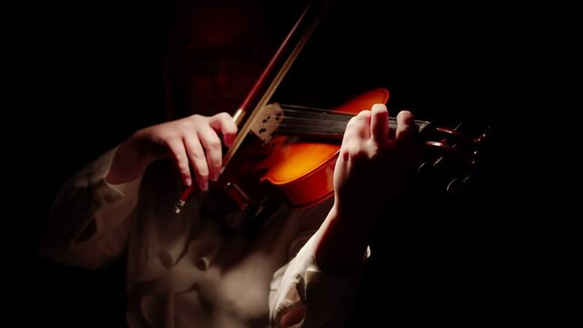 Woman comes out of darkness studio and puts a bow on strings of the violin begins to play the classical melody. Concept symphony orchestra.