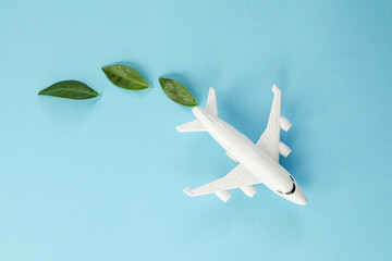 Sustainable Aviation Fuel. White airplane model, fresh green leaves on blue background. Clean and...
