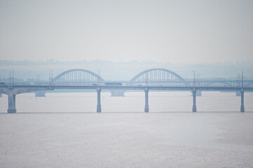 View of the railway and road bridges over a wide river, filmed on a cloudy, foggy day.