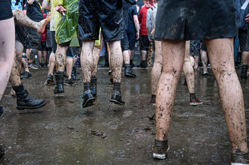 Dirty legs of people dancing in the mud during concert. - obrazy, fototapety, plakaty