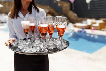 Midsection of waiter offering champagne at poolside.Serving with ice on a tray. Swimming pool party concept.