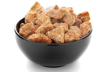 Close-Up of organic sugarcane jaggery piece in black ceramic bowl over white background