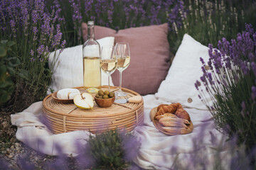 Beautiful picnic with wine, cheese, olives, ciabatta bread and croissants in a lavender field.