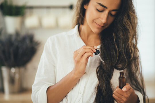 Young woman applying natural organic essential oil on hair and skin. Home spa and beauty rituals.
