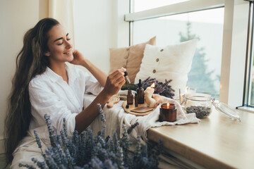 Young woman applying natural organic essential oil on hair and skin. Home spa and beauty rituals.