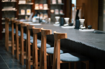 Selective focus in front of wooden seat with coffee counter and blur coffee making equipment background. design for cafe or home