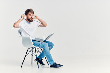 man in white t-shirt sitting on a chair with a laptop in headphones