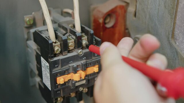 Closeup. Electricians hands testing current electric in control panel. Electrician engineer work tester measuring voltage and current of power electric line in electical cabinet control.