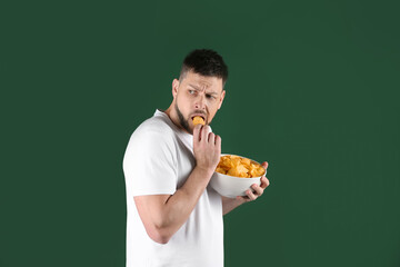 Greedy man hiding bowl with chips on green background