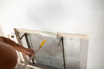 Fototapeta na wymiar White paint roller in hand with drywall wall.