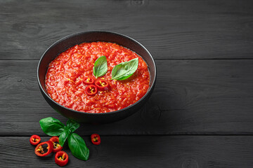 Spicy tomato sauce with basil in a bowl on a black background.