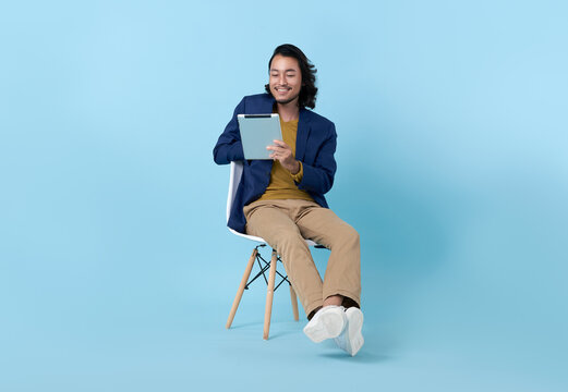 Businessman asian happy smiling using a digital tablet while sitting on chair isolated on bright blue background..