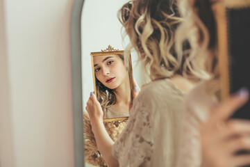 Young beautiful model girl with natural makeup looks at her reflection in the mirror