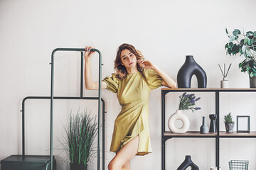 Young model girl in a dress in a room with shelves and plants in a home interior