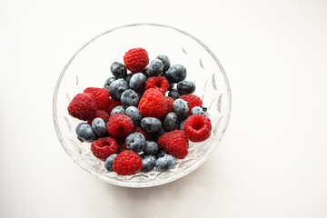 raspberries and blueberries in a transparent bowl on a white background