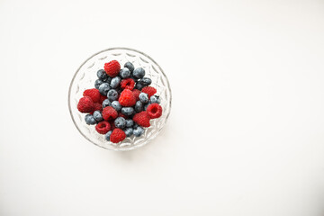 raspberries and blueberries in a transparent bowl on a white background