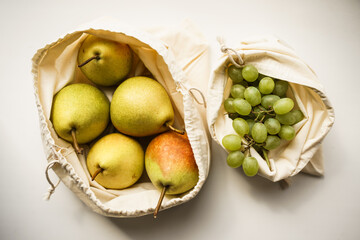 pears and grapes in white linen eco bags on a white windowsill