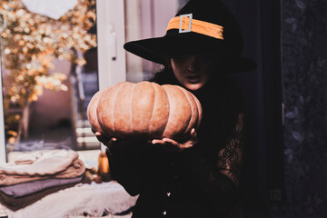 Halloween lady wearing witch cup. A woman in witch hat and Halloween pumpkin near the windows....