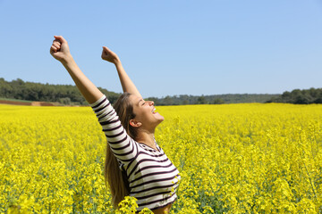 Excited woman raising arms in a yellow field celebrating spring