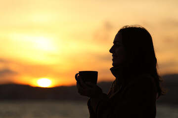 Silhouette of a woman holding coffee mug at sunset on the beach