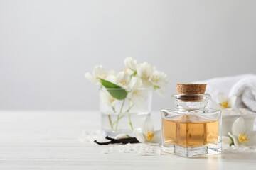 Beautiful composition with jasmine essential oil and fresh flowers on white wooden table. Space for text