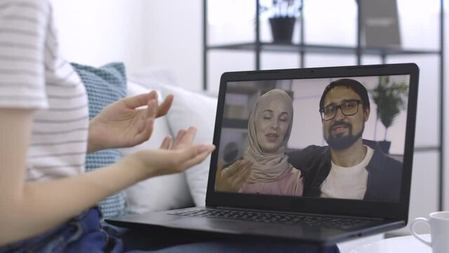 Close up of laptop screen with pleasant young Arab couple having a video call with their Caucasian female friend. Woman communicates via online video call, gesturing while talking with friends