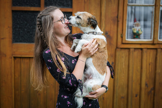 Kleiner Terrier Hund schleckt einer jungen Frau mit Brille &uuml;bers Gesicht. Freundschaft, Liebe. auf dem Arm.
