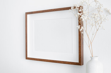Horizontal frame with passepartout on white wall with dry gypsophila plant in vase. Blank mockup...