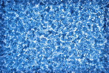 Ice and frost crystals on the window pane close up. Blue tinted wallpaper. Unusual festive background for winter, Christmas or New Year. Backdrop looks like a bunch of broken glass fragments. Macro
