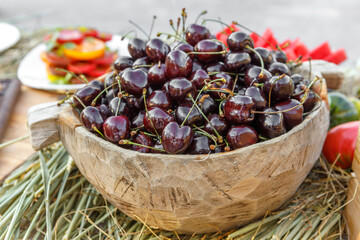 Ripe cherries are lying in a wooden cup on the table.