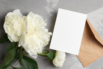 Obraz na płótnie Canvas Greeting card mockup with copy space and white peony flowers and envelope on grey