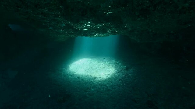 A beam of light enters the underwater cave through a hole in the ceiling. 4K - 60 fps. Cave diving in Mediterranean Sea, Cyprus