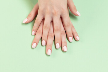 Female hands with pink nail polish applied on a light green background. Perfect artificial fingernails of young woman. Selective focus	