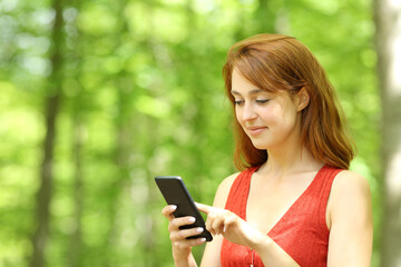 Woman checking phone walking in a green park