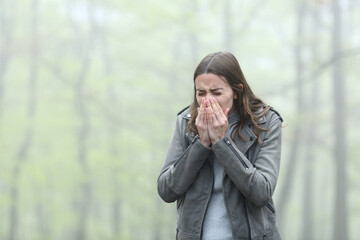 Woman sneezing in a cold foggy park